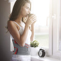 Woman by window wearing ORTONYX lumbosacral lumbar support belt back brace, breathable knitted lumbar belt with red accents.