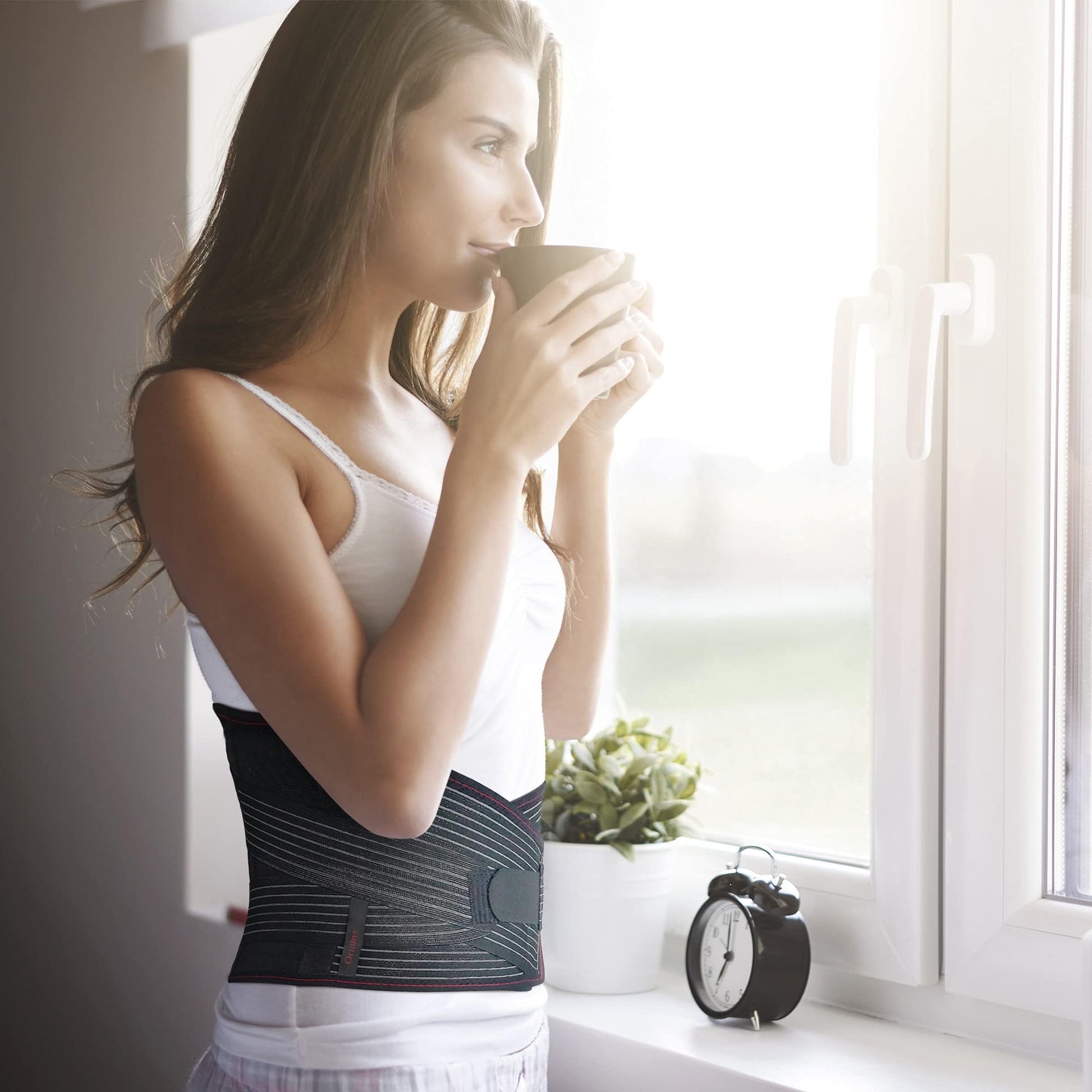 Person sipping coffee at window wearing ORTONYX lumbosacral lumbar support belt back brace, breathable knitted lumbar belt.