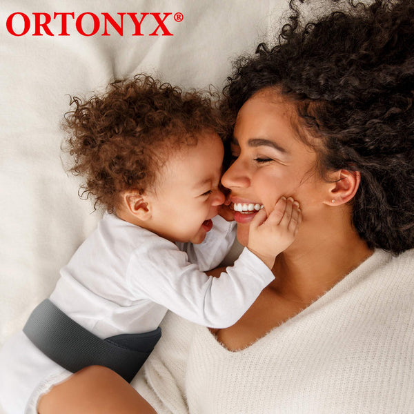 Smiling baby wearing ORTONYX infant umbilical hernia belt OX350; gray pediatric hernia truss around navel while cuddling mom