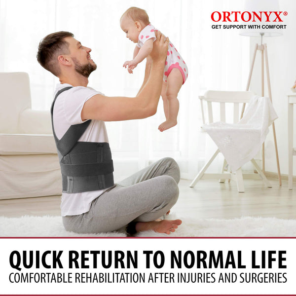 Man wearing ORTONYX Comfort Posture Corrector 656 clavicle and shoulder support back brace, lifting a baby in a living room